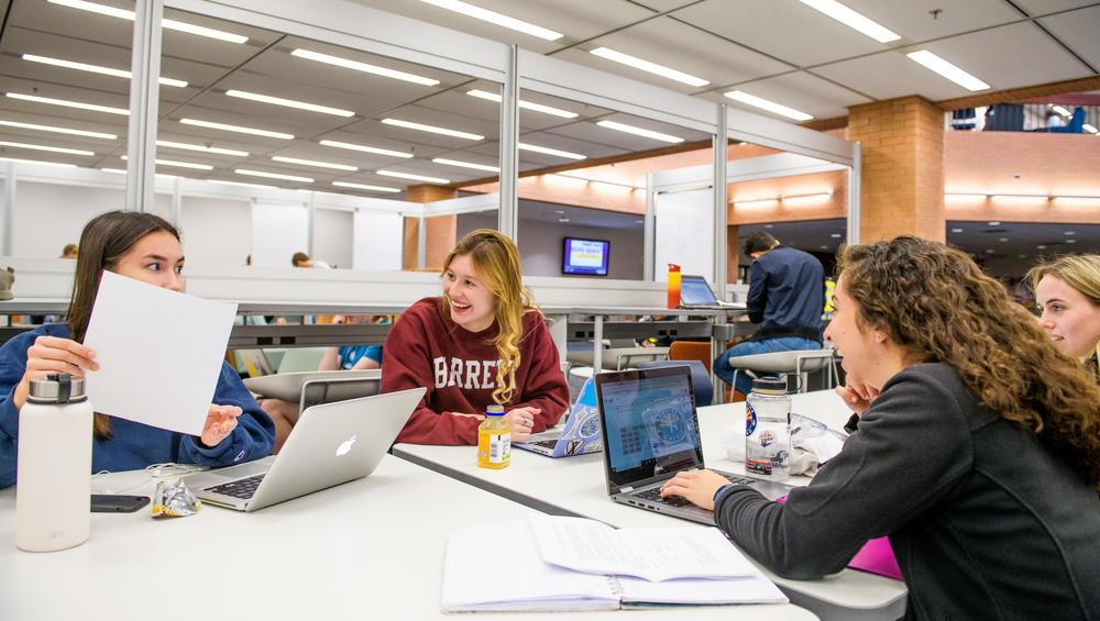 Smiling ASU students in discussion at their laptops in class.