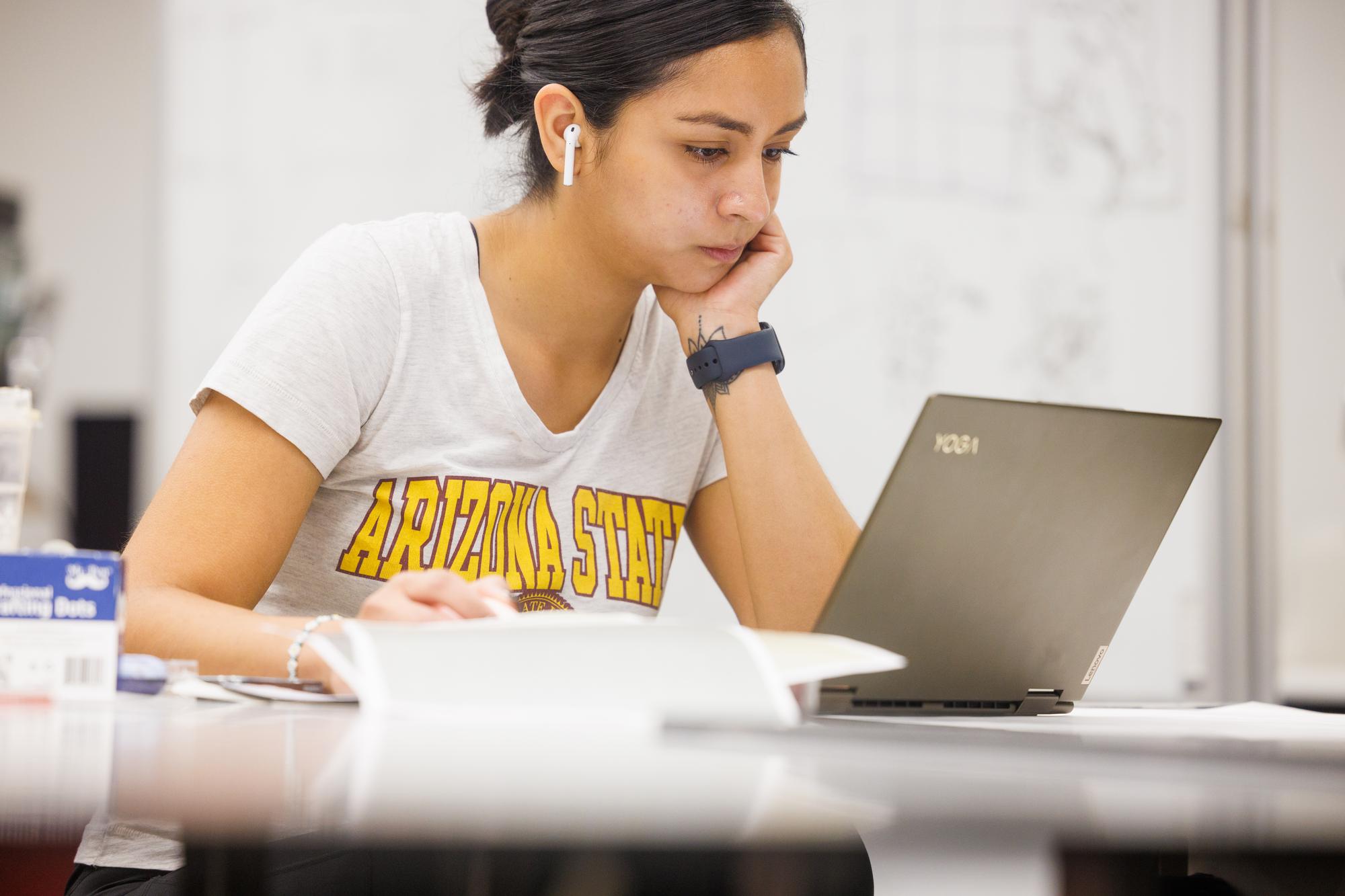 A female student wearing earbuds looks at her laptop screen in concentration.