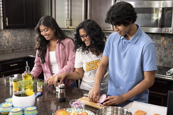 ASU student and two others happily cooking in a kitchen at home.