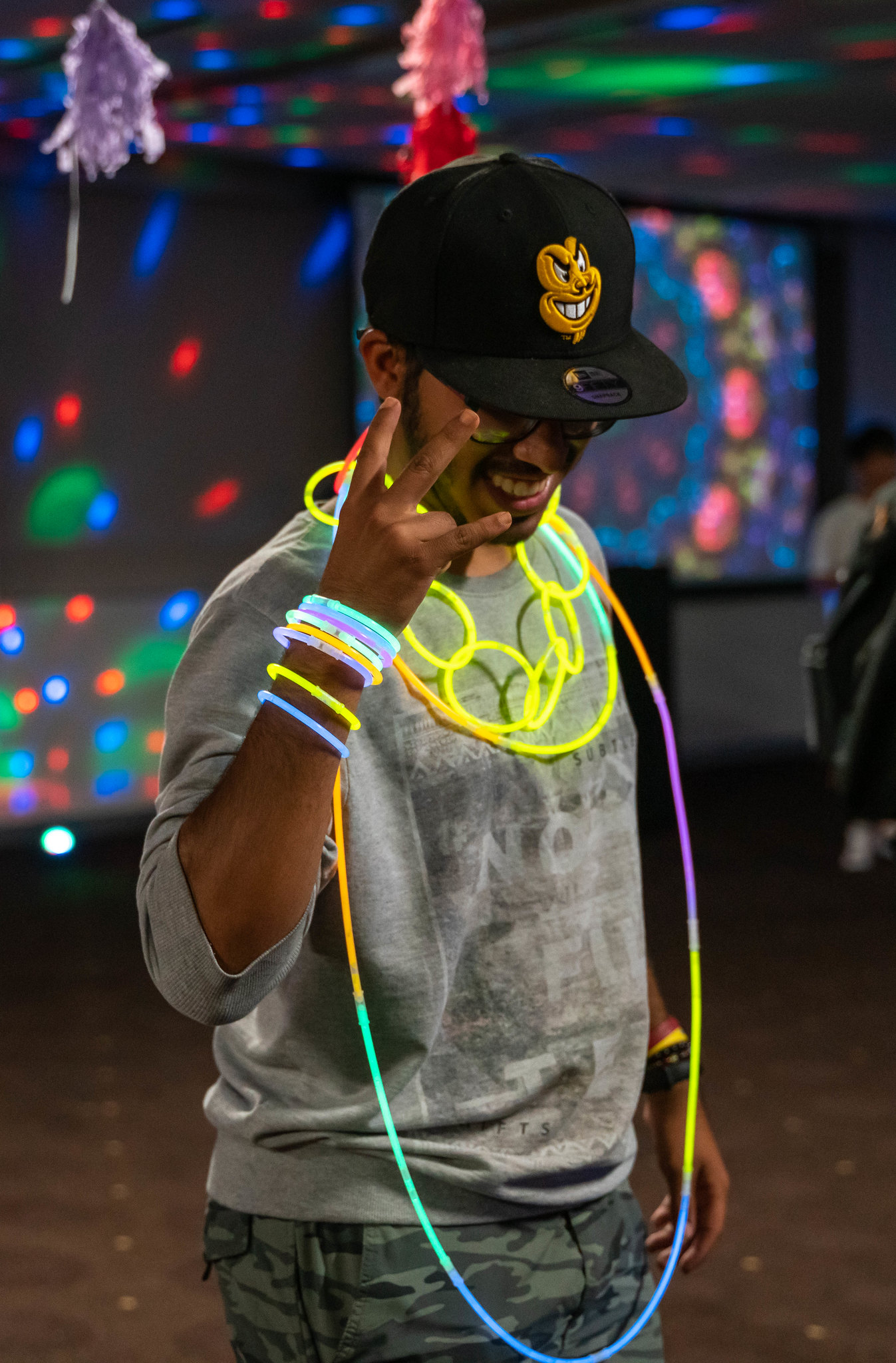 A student posing in blacklight highlighting colorful glow sticks and accessories.