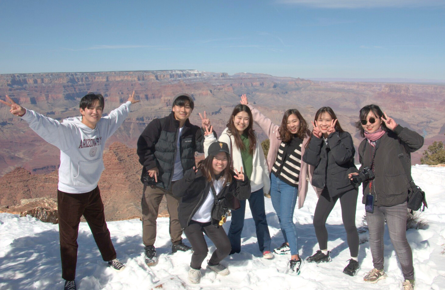 Students posing, giving peace signs in snow at Grand Canyon.