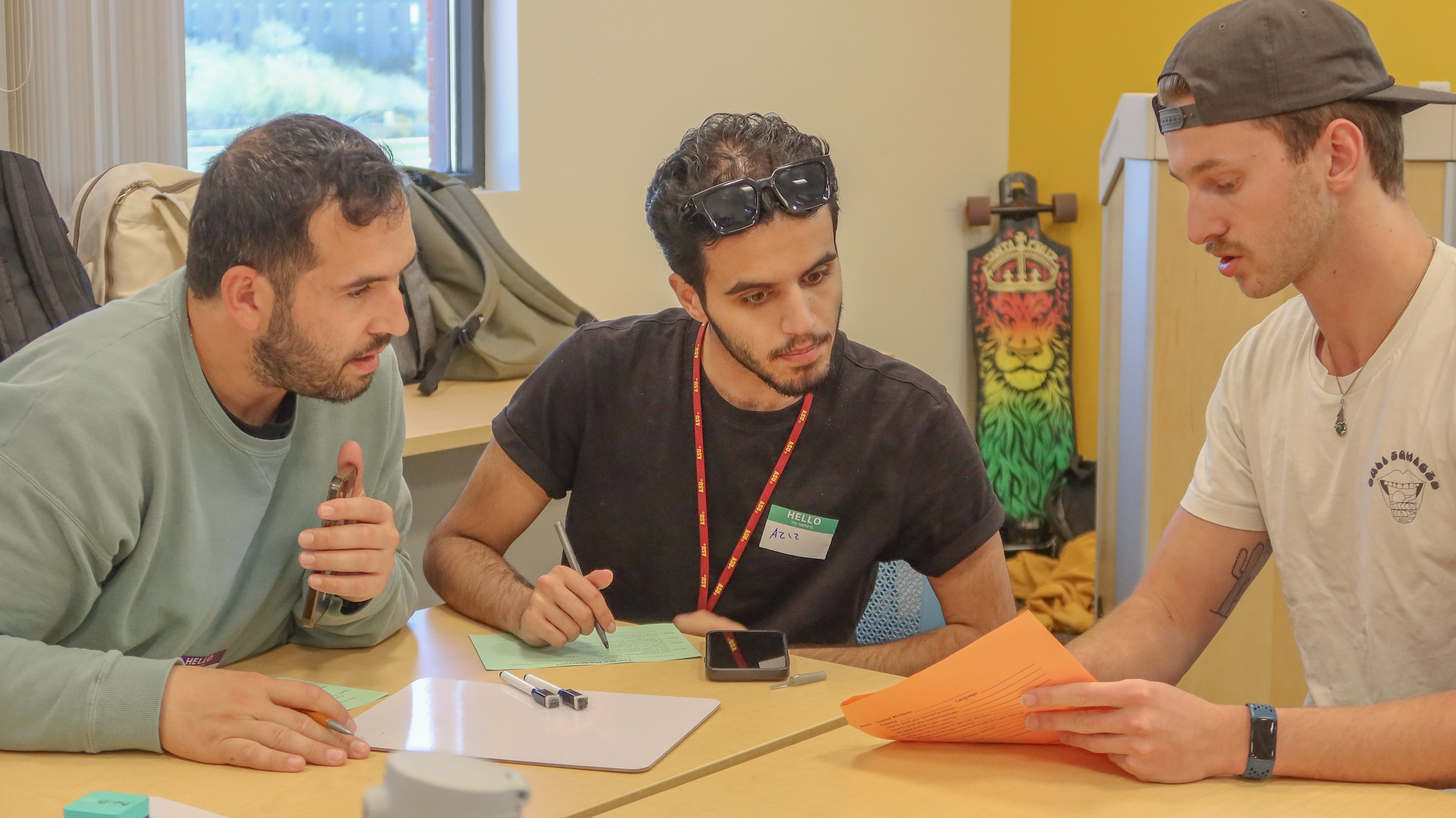 Two male students look at the writing on a paper that a third student is showing them.