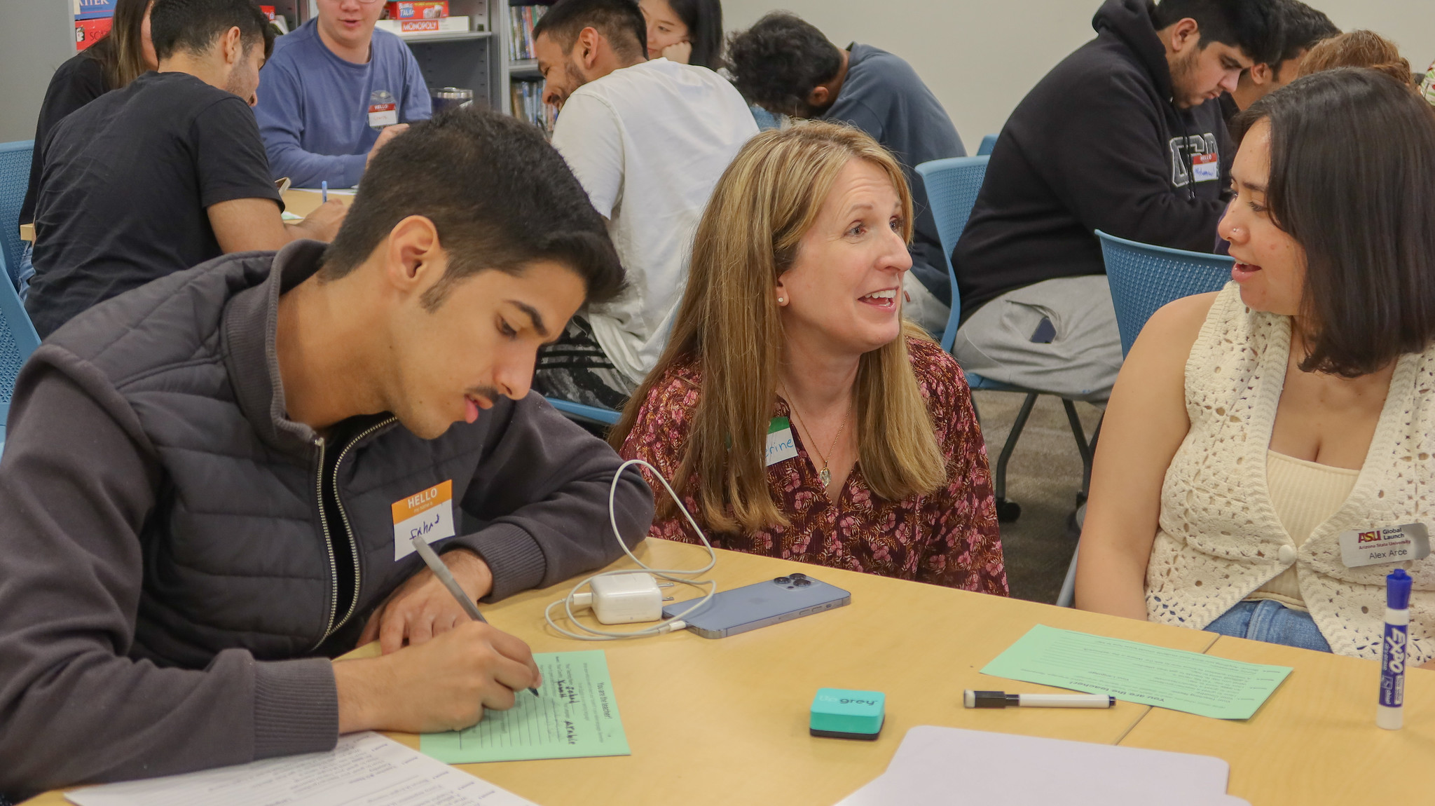 An instructor speaks with a student while another is taking notes.