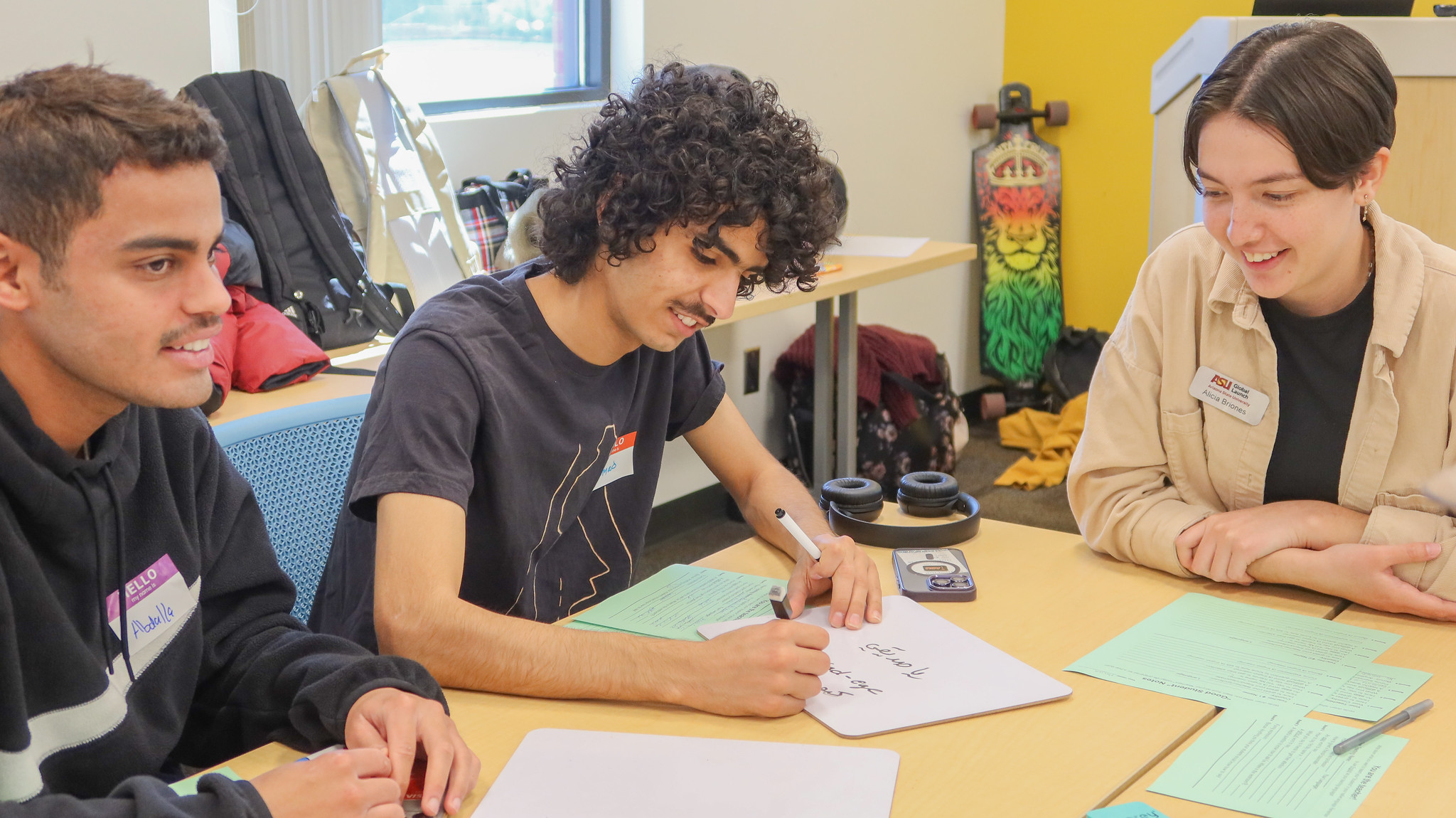 A student looks at another student writing something on a whiteboard.