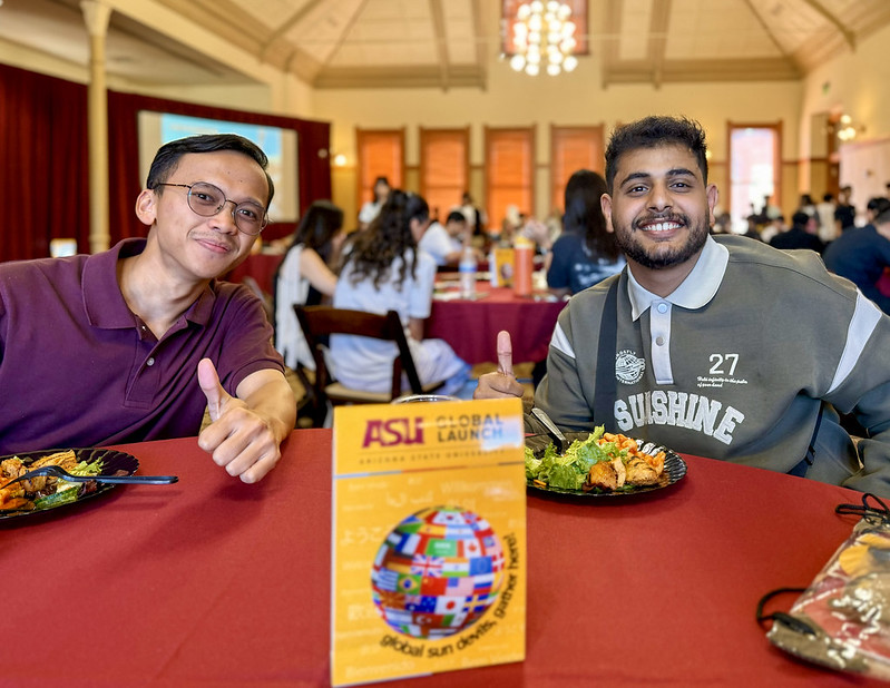 Two students give thumbs up at table while eating lunch.