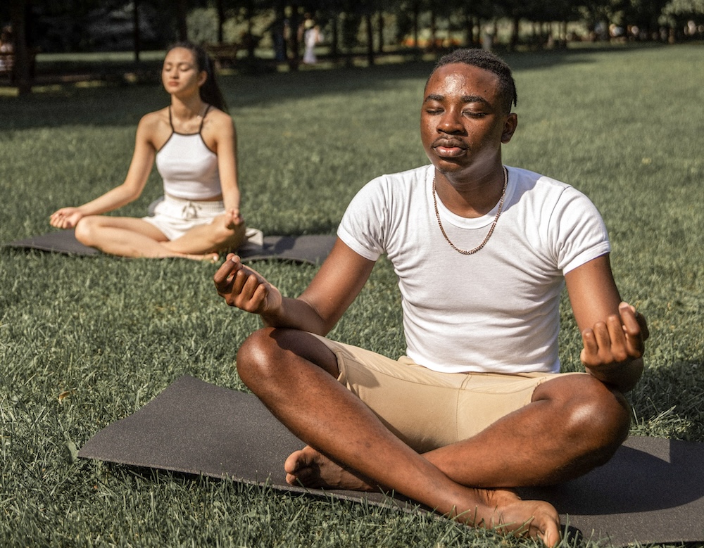 A young man and woman sitting lotus style, meditating outdoors. Photo by Monstera Production via Pexels