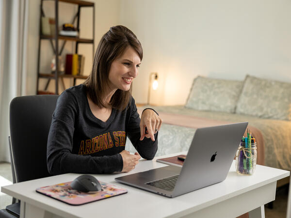 Smiling ASU student studying on her laptop in her bedroom.