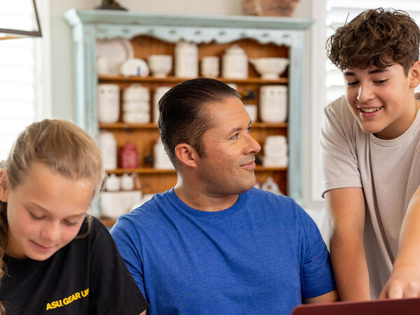 Man helping two younger students at a laptop and workbook.