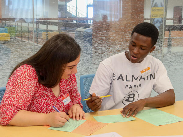 Two students discussing their work writing down answers in a classroom.