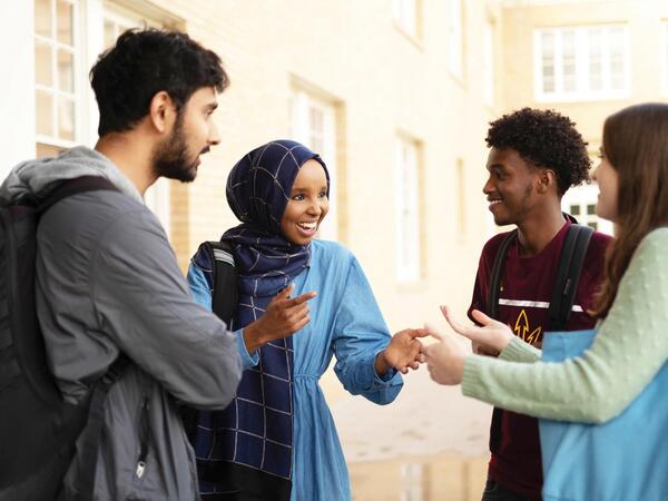 Smiling group of students standing in circle enjoying conversation.