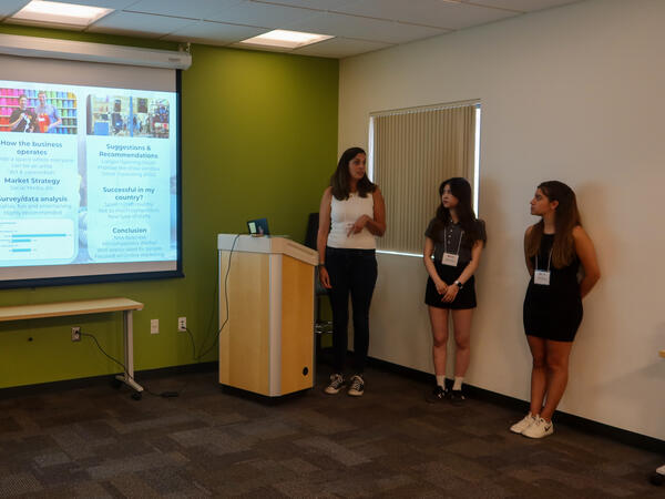 Four people presenting in a classroom with a projector screen displaying a slide.