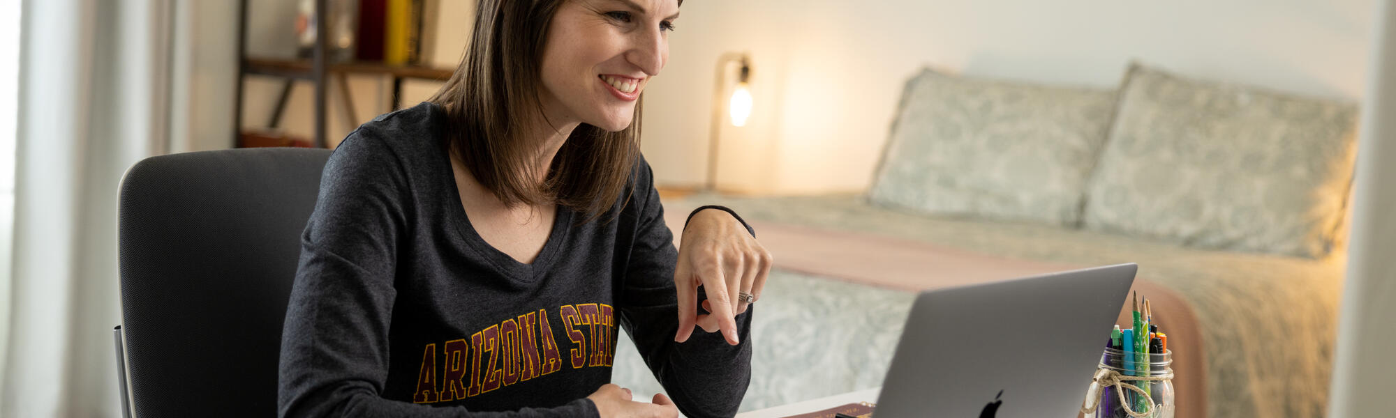 Smiling ASU student studying on her laptop in her bedroom.