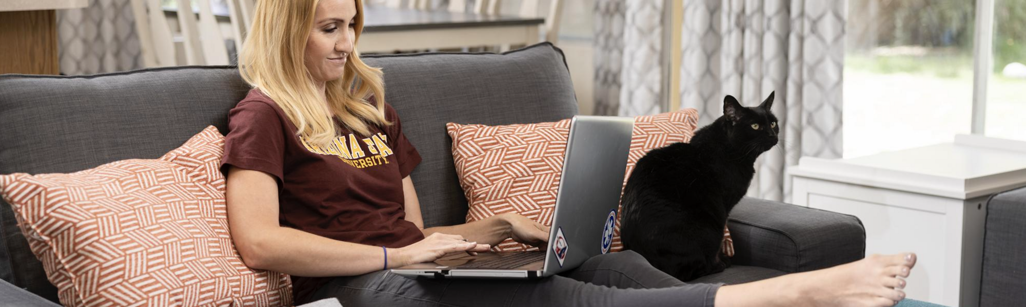 An ASU student sits on her couch with her laptop and cat for her online class.