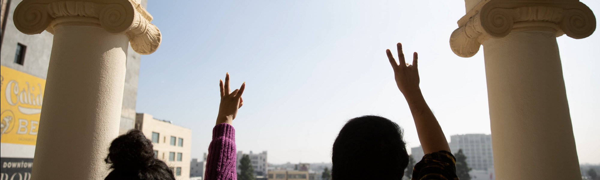 Two ASU students holding up the pitchfork symbol looking out toward campus.