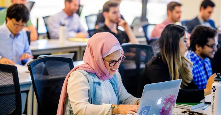 A smiling ASU student at her laptop in class.