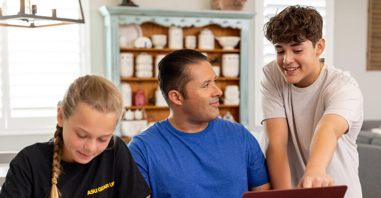 Man helping two younger students at a laptop and workbook.