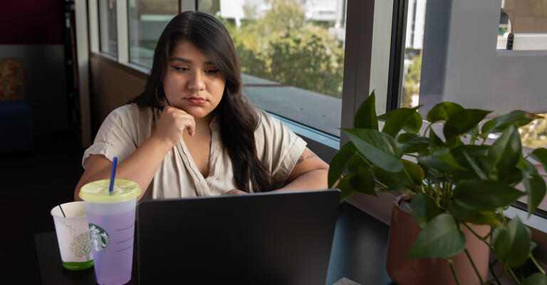 A female student gazing forlornly at her laptop in thought.