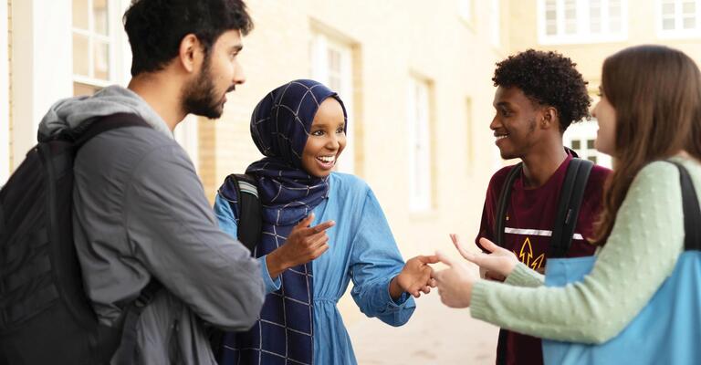 Smiling group of students standing in circle enjoying conversation.