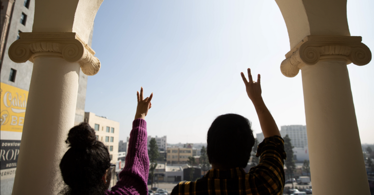 Two ASU students holding up the pitchfork symbol looking out toward campus.