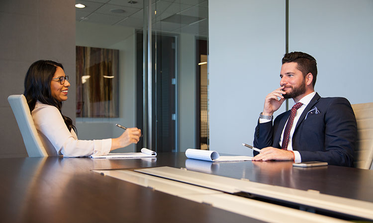 Two employees discuss topics at a business meeting inside a conference room