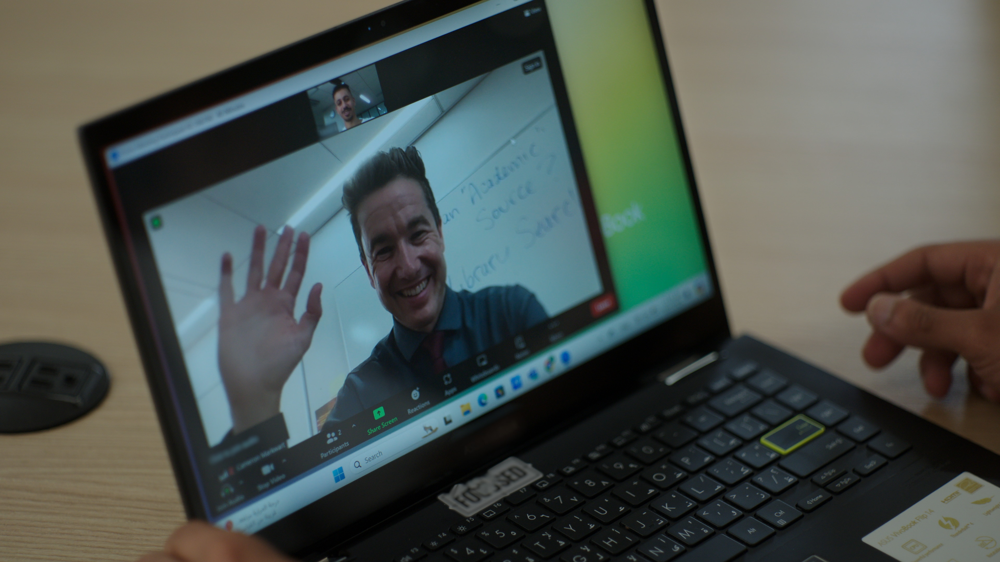 Laptop displaying a video call with a man smiling in front of a whiteboard.