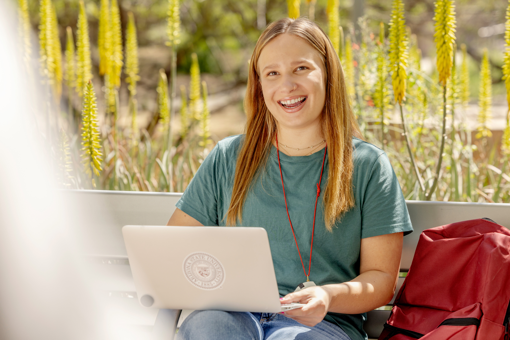 Smiling student with laptop sitting outside on a bench.