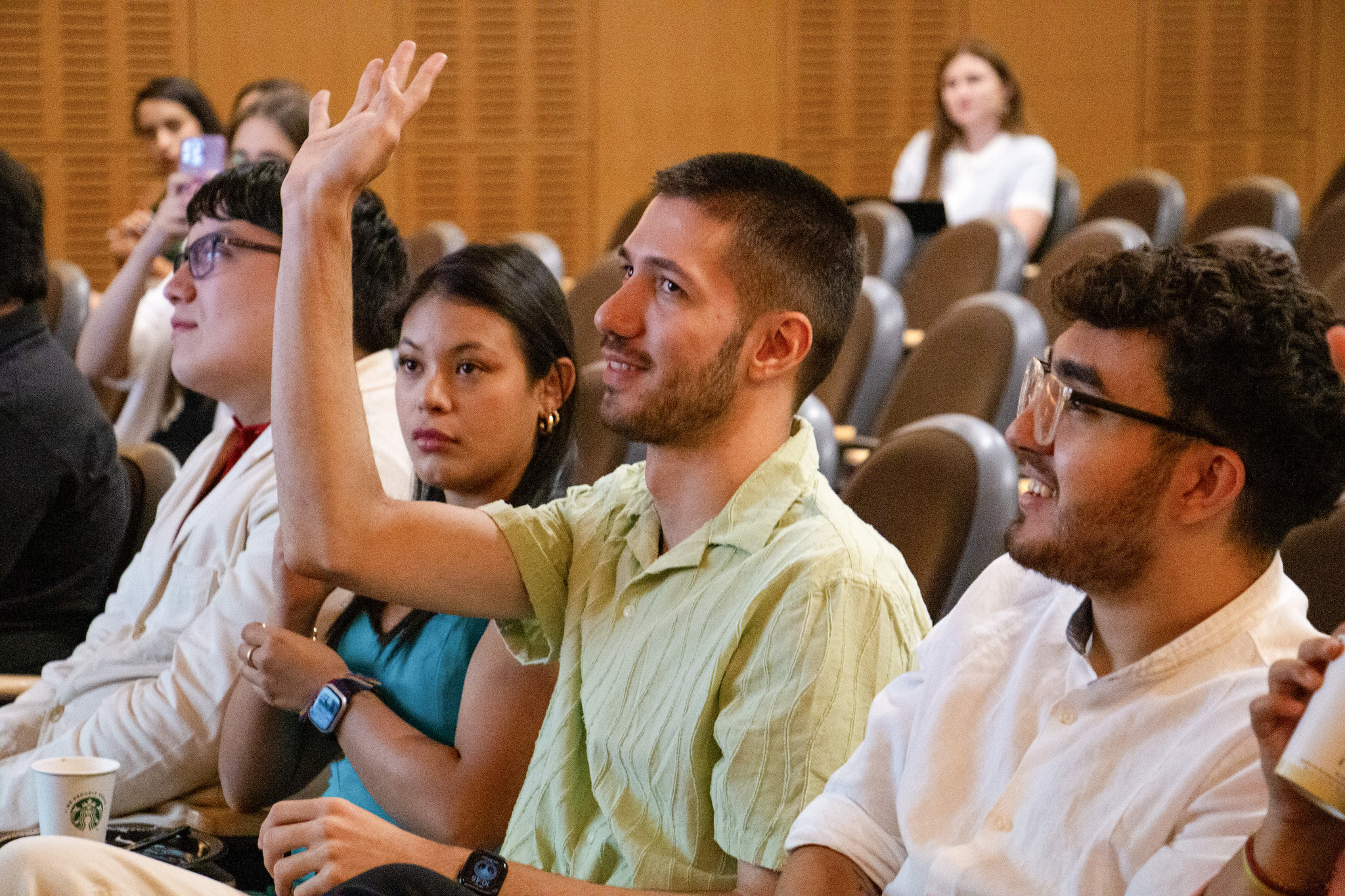 Students sitting watching a presentation with one raising his hand.