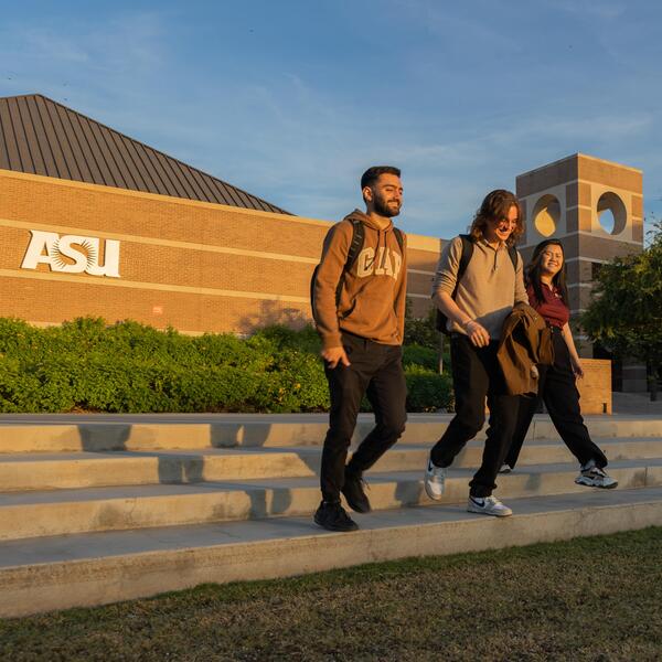 Three young adults walk down steps on a university campus with an ASU building in the background during sunset.