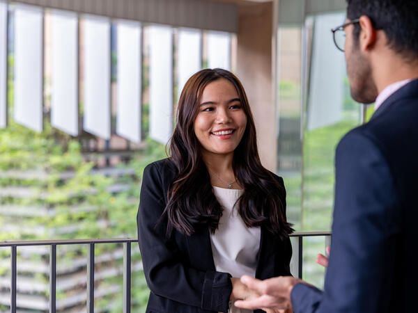 Female student in business attire smiling and shaking another businessman’s hand.