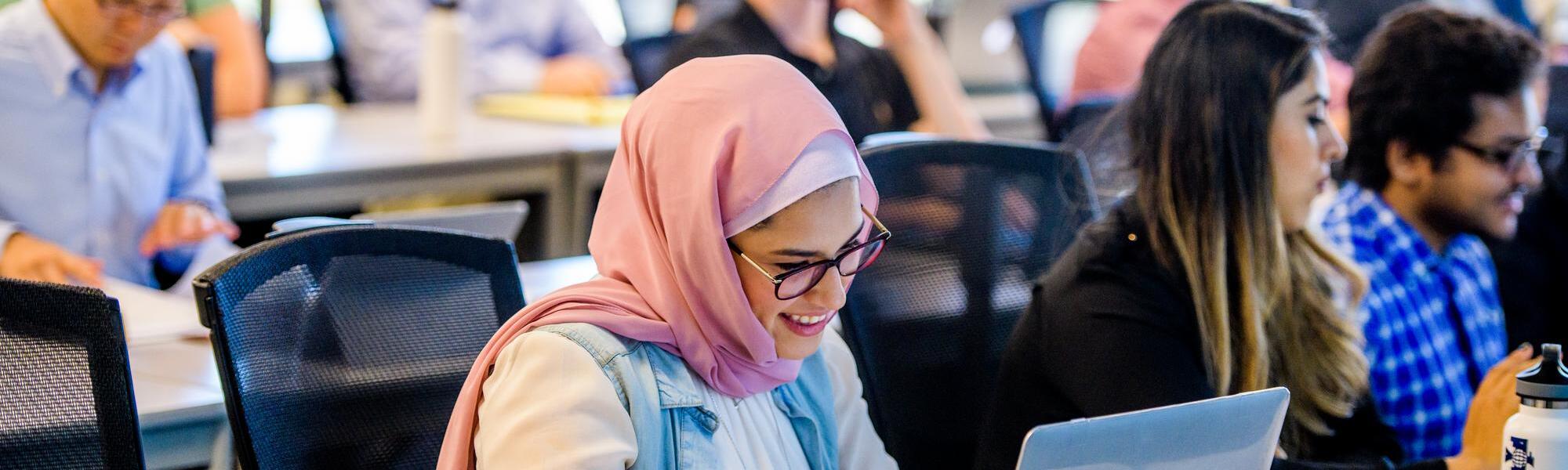 A smiling ASU student at her laptop in class.