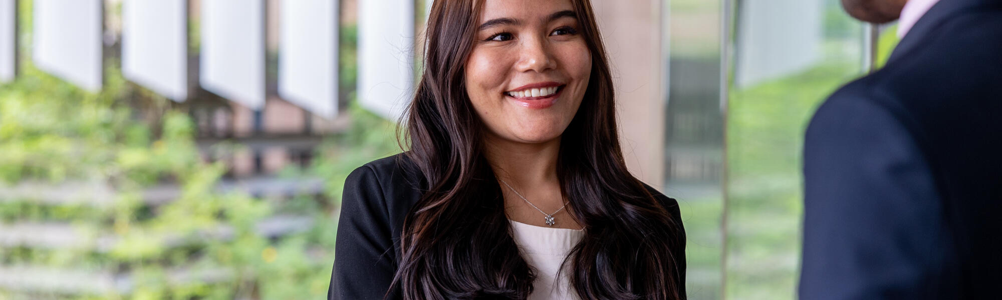 Female student in business attire smiling and shaking another businessman’s hand.