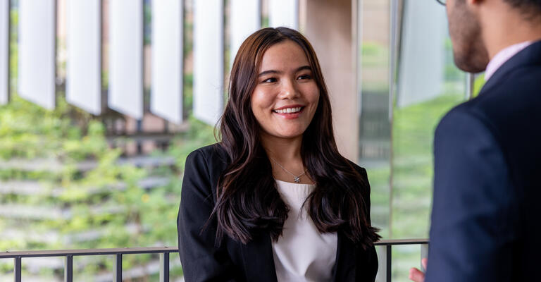 Female student in business attire smiling and shaking another businessman’s hand.