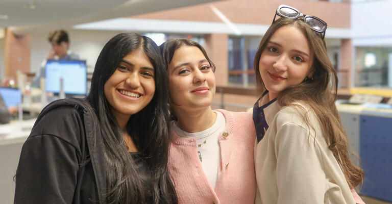 Three female ASU students pose together near the Global Launch Welcome Desk.